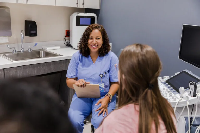 A woman in scrubs speaks to a patient in an exam room